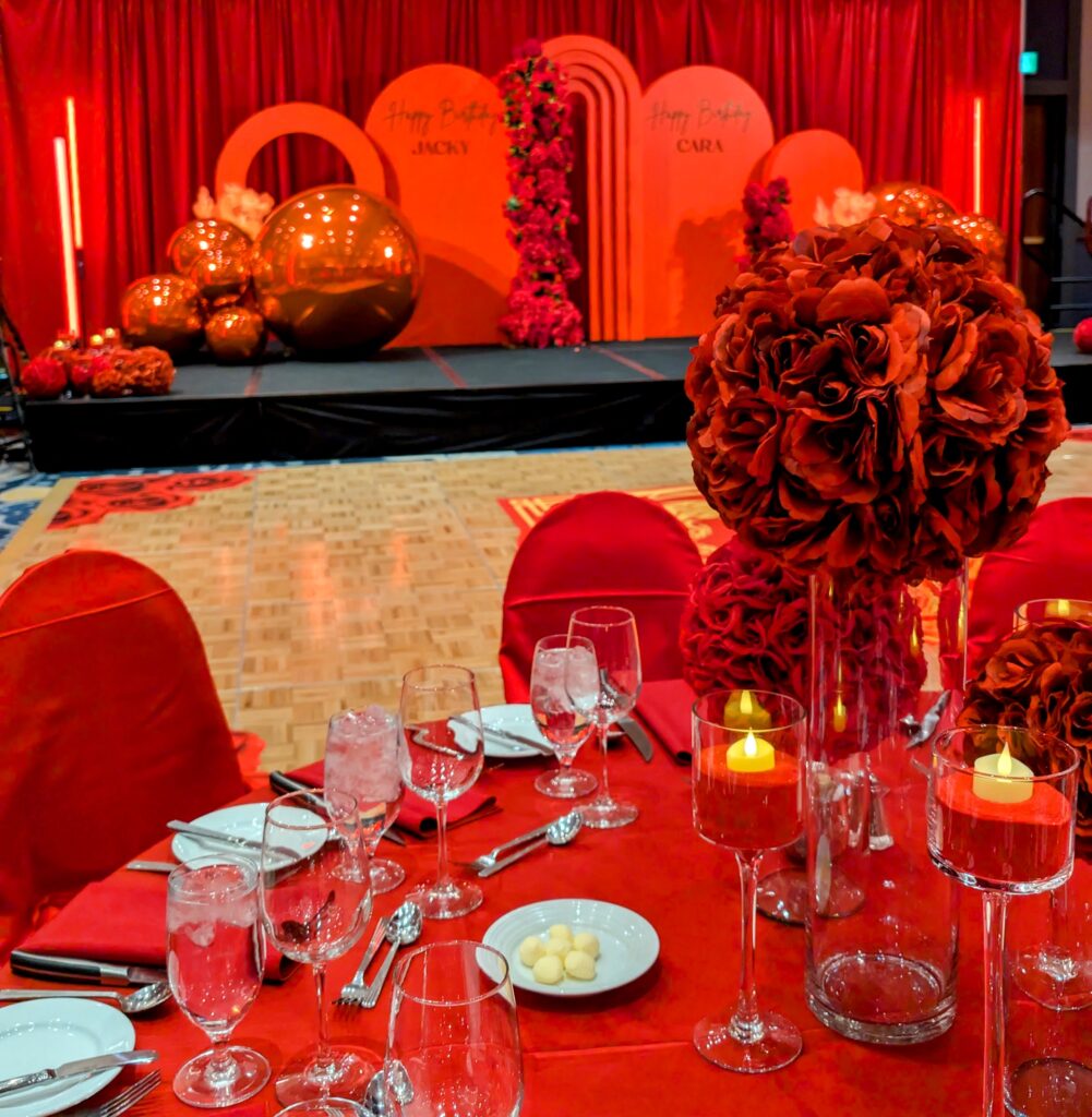 red flower balls on glass vases with red sand and candles in glass stemmed votives